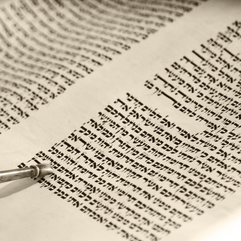 Close-up of a Torah scroll with Hebrew text and a yad (pointer) following the lines.