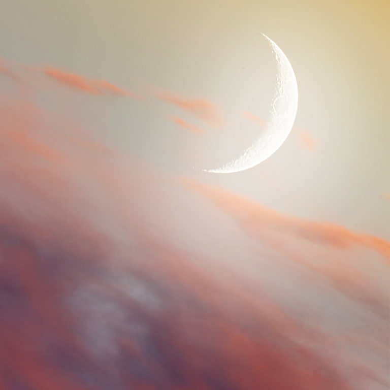 A crescent moon in a soft, pastel sky with pink and orange clouds at dusk or dawn.