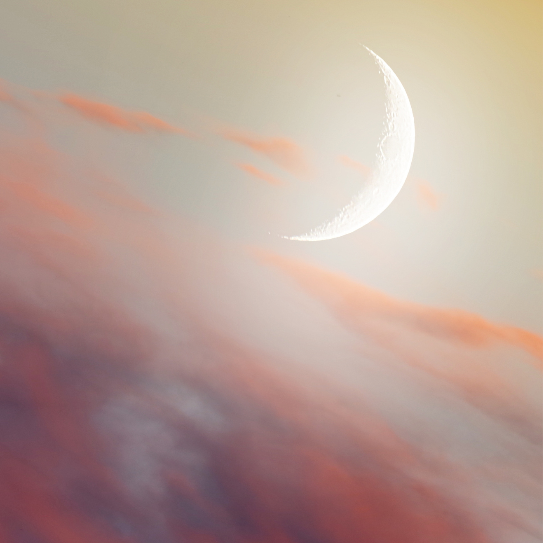 Crescent moon against a soft, colorful sky with pink and orange clouds.