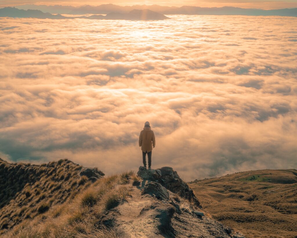 person standing on mountain in front of sea of clouds and sunshine