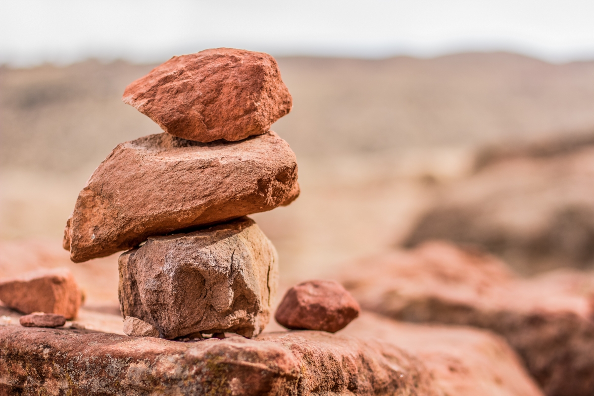 Stacked reddish-brown stones balanced on a rock in a desert landscape.