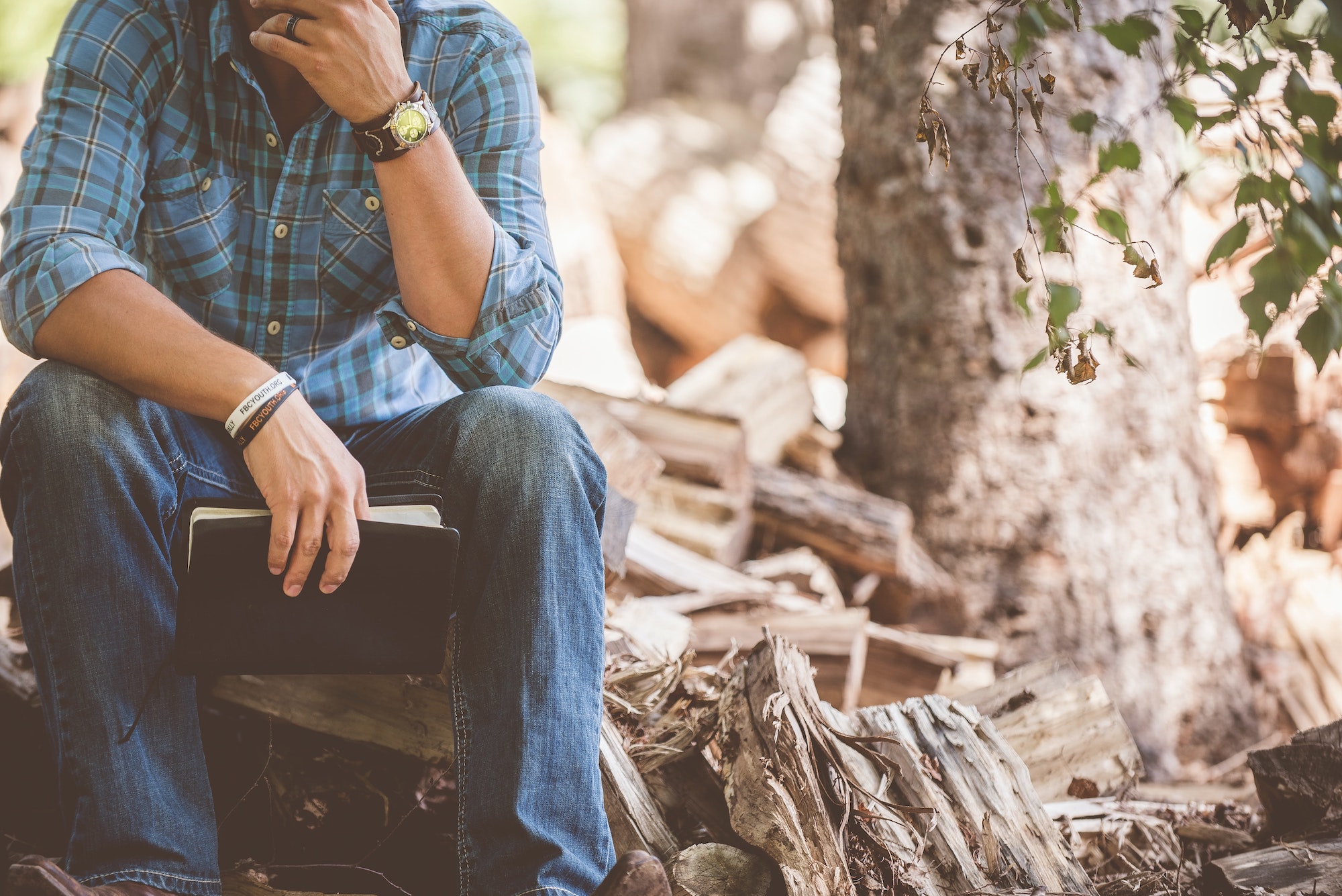 man holding book sitting on log appearing to be contemplative