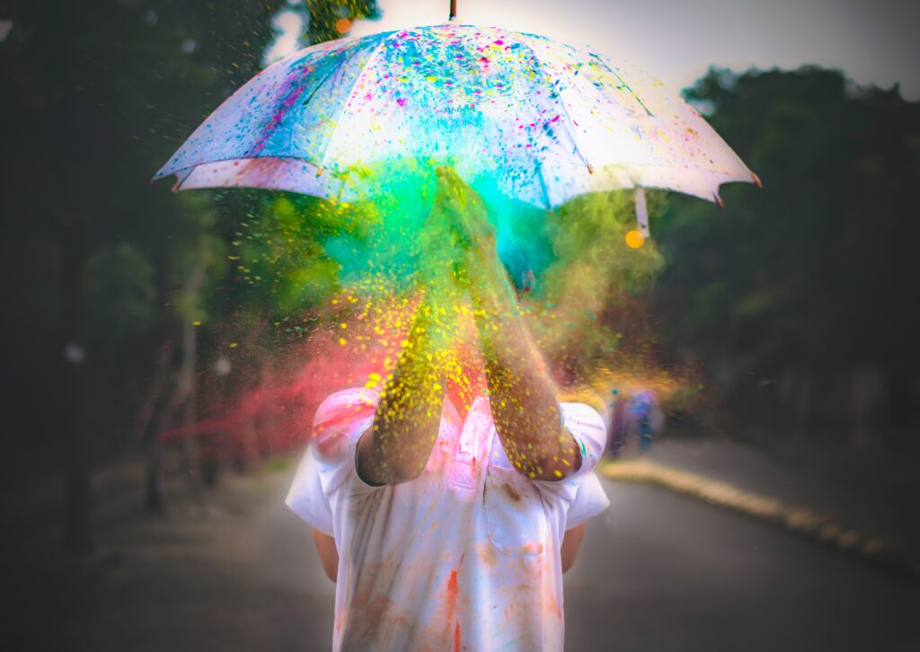 person holding white umbrella with multi-colored paint or sparkles raining down over them