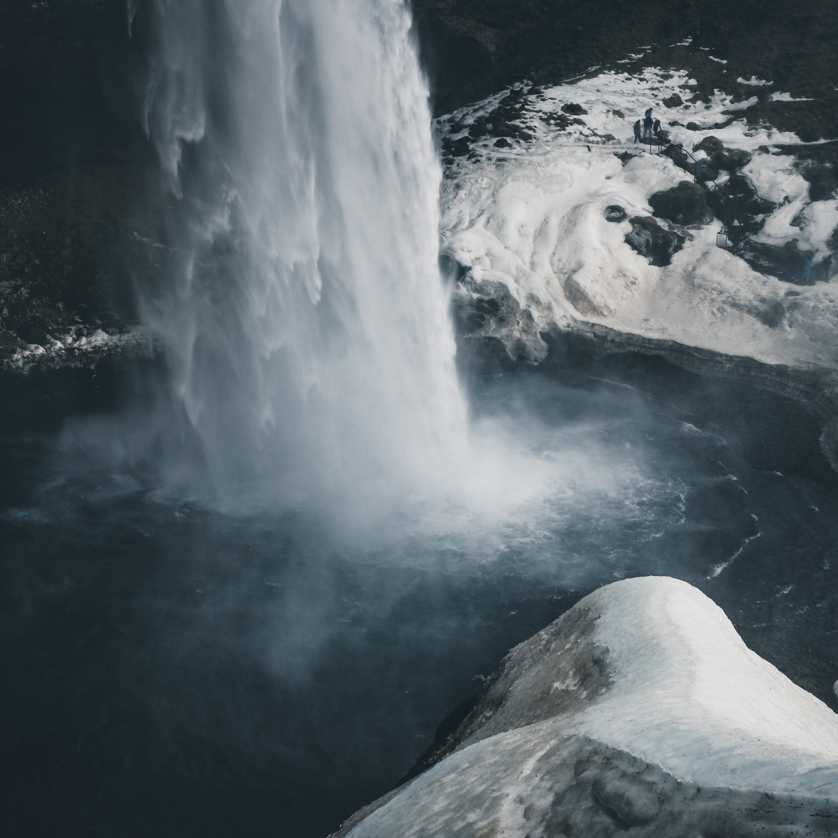 Aerial view of a waterfall cascading into a pool, surrounded by icy terrain.