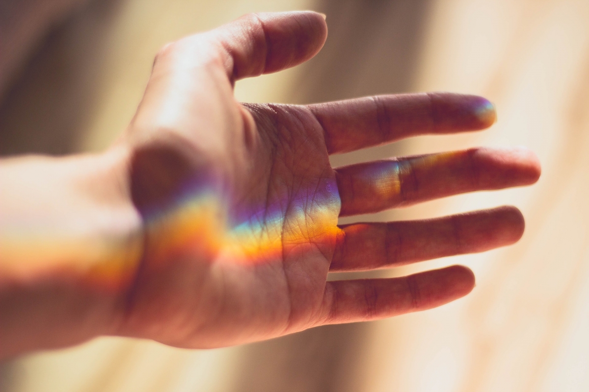 An open hand with a rainbow light pattern across the palm, set against a soft-focus background.