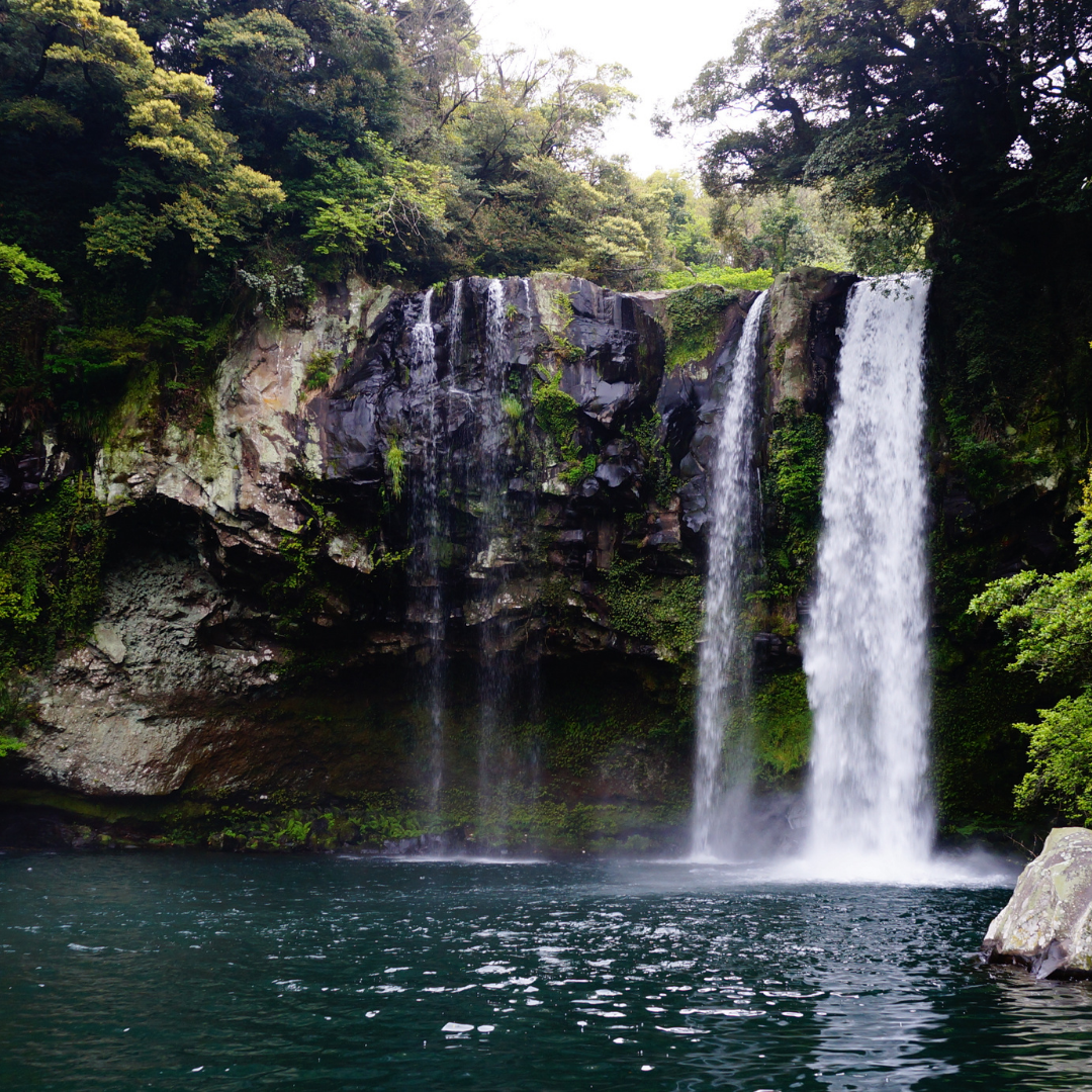 Waterfall cascading into a tranquil pool surrounded by lush greenery and rocky cliffs.