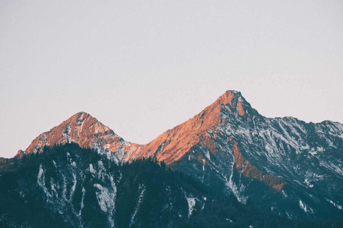 Two snow-capped mountains at sunset with warm orange light casting on the peaks.