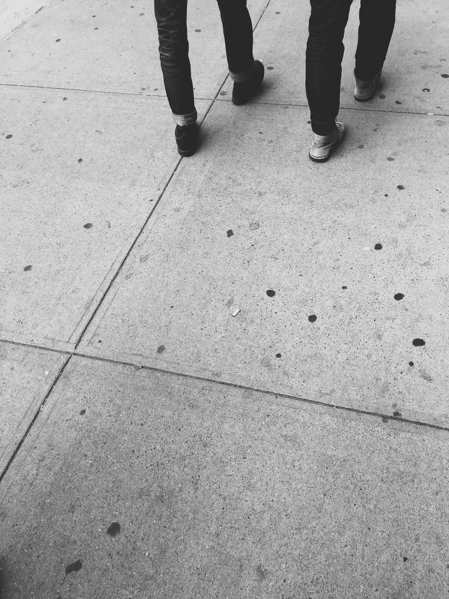 Black and white image of two people walking on a concrete sidewalk.