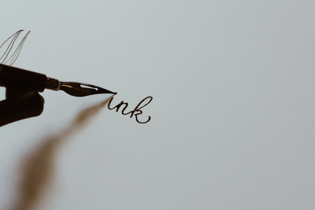 Close-up of a calligraphy pen writing the word ink on white paper.