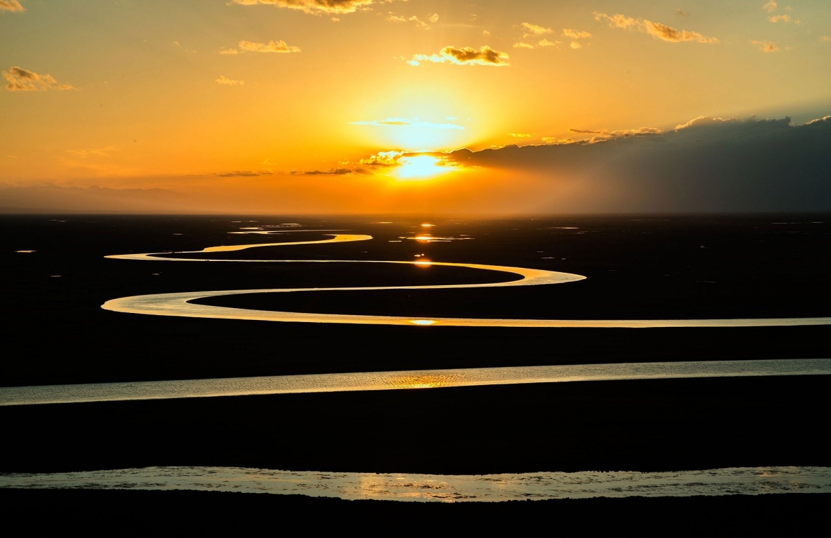 Sunset over a winding river with a golden sky and scattered clouds.