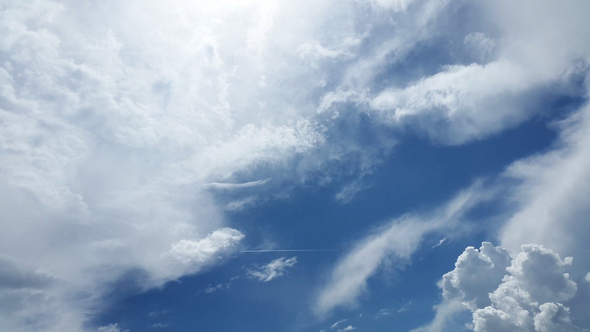 Blue sky with scattered white clouds and sunlight streaming through.