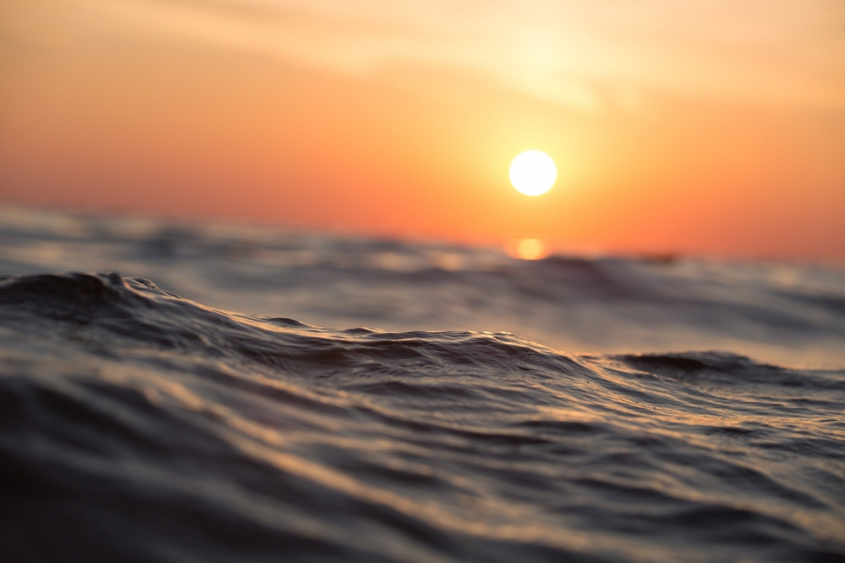 Sunset over a calm ocean, with the sun casting an orange glow on the rippling waters surface.