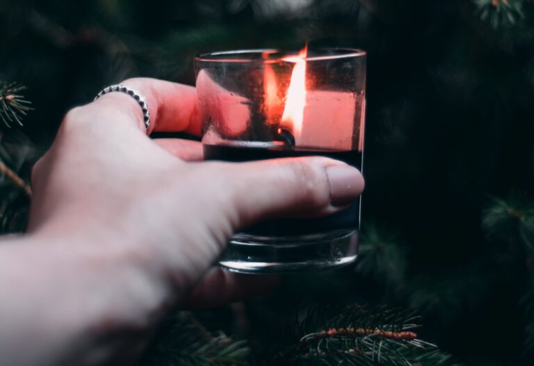 close up of white hand holding lit candle in glass holder