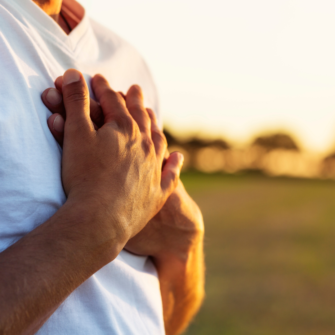 close up of person's hands on their chest outdoors in sunlight