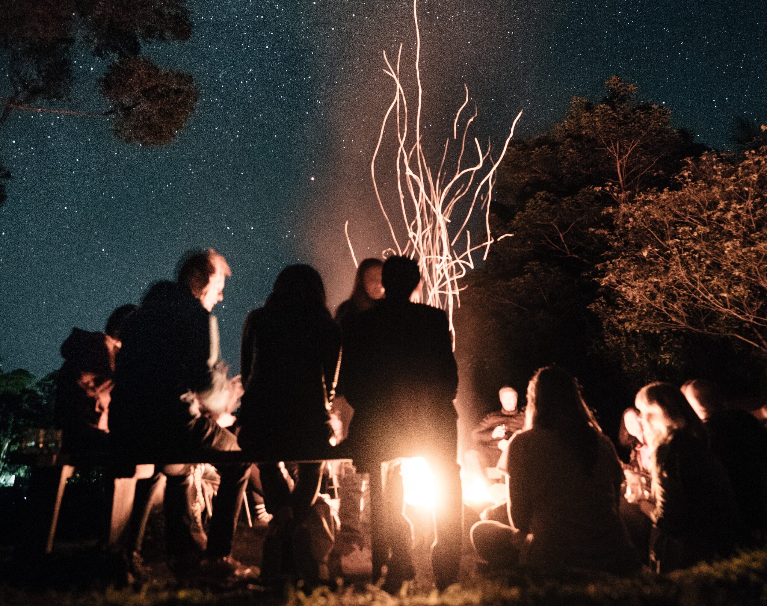 group of people sitting around bonfire under night sky, their faces glowing
