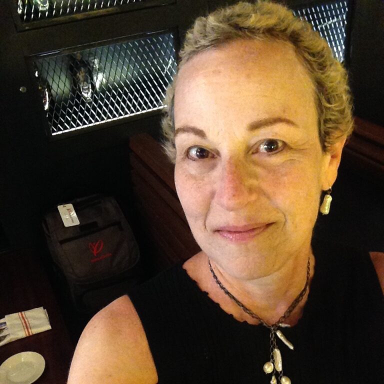 A person with short blonde hair takes a selfie in front of a locker with a bag inside.