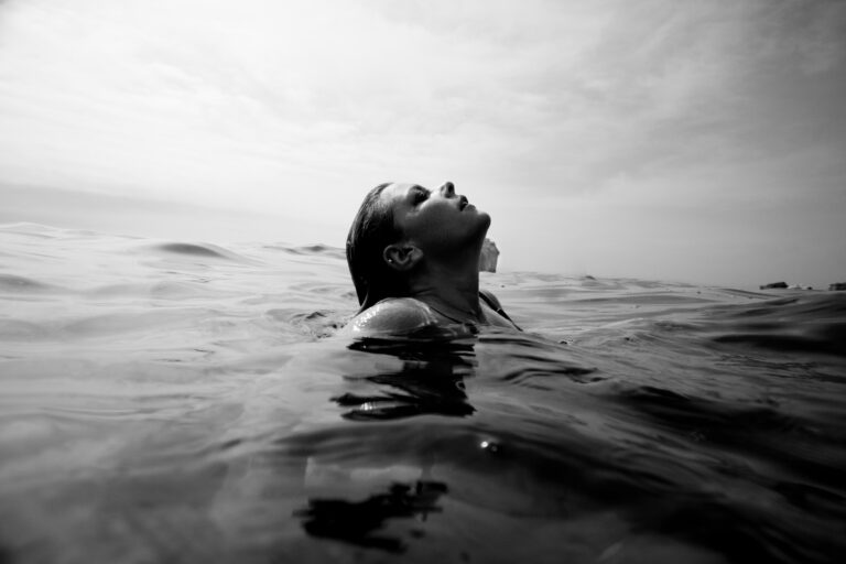 black and white photo of white woman immersed in ocean water, head sticking out the water, leaning back, eyes closed