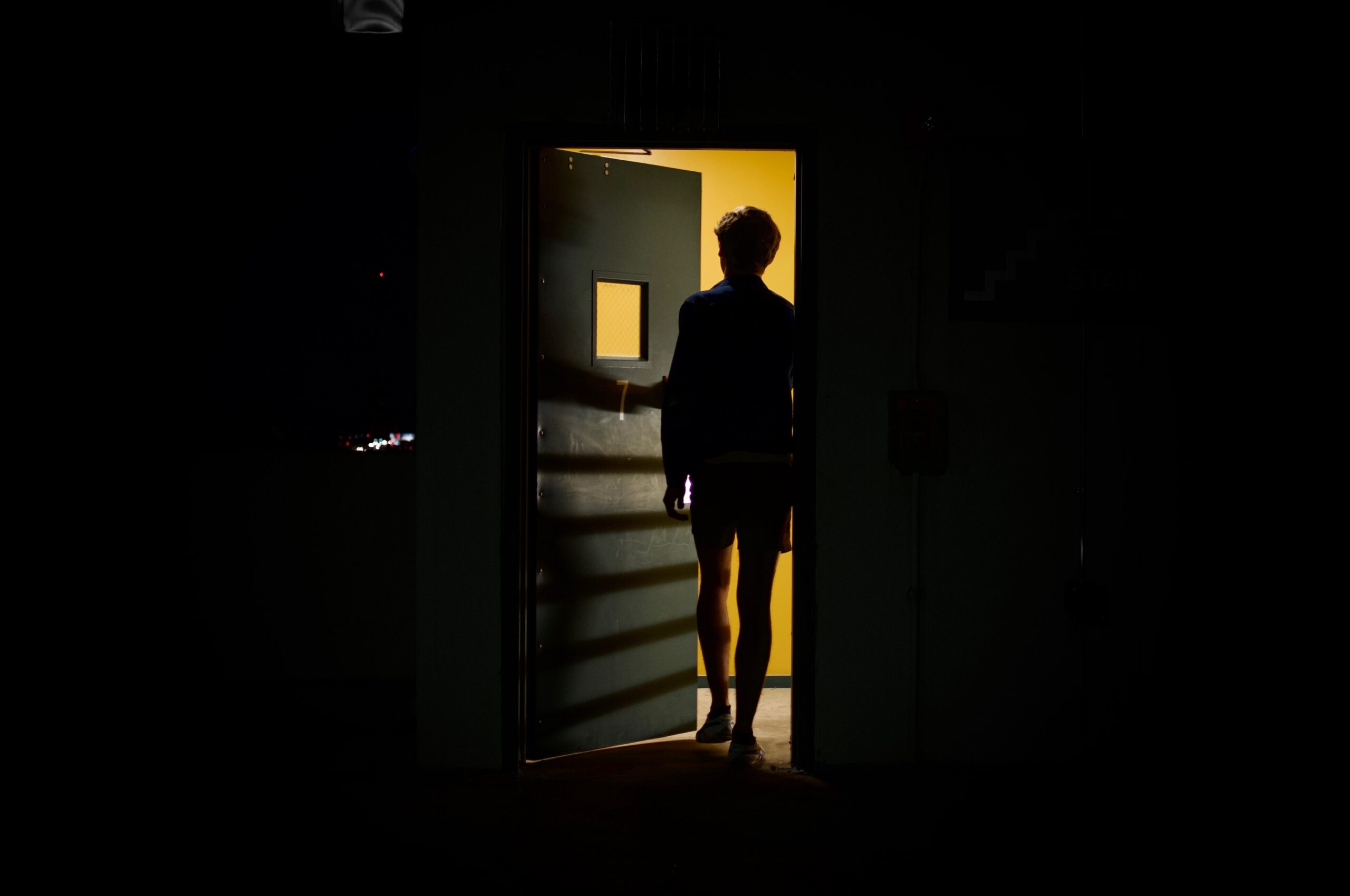 dark photo of person walking through door with yellow light
