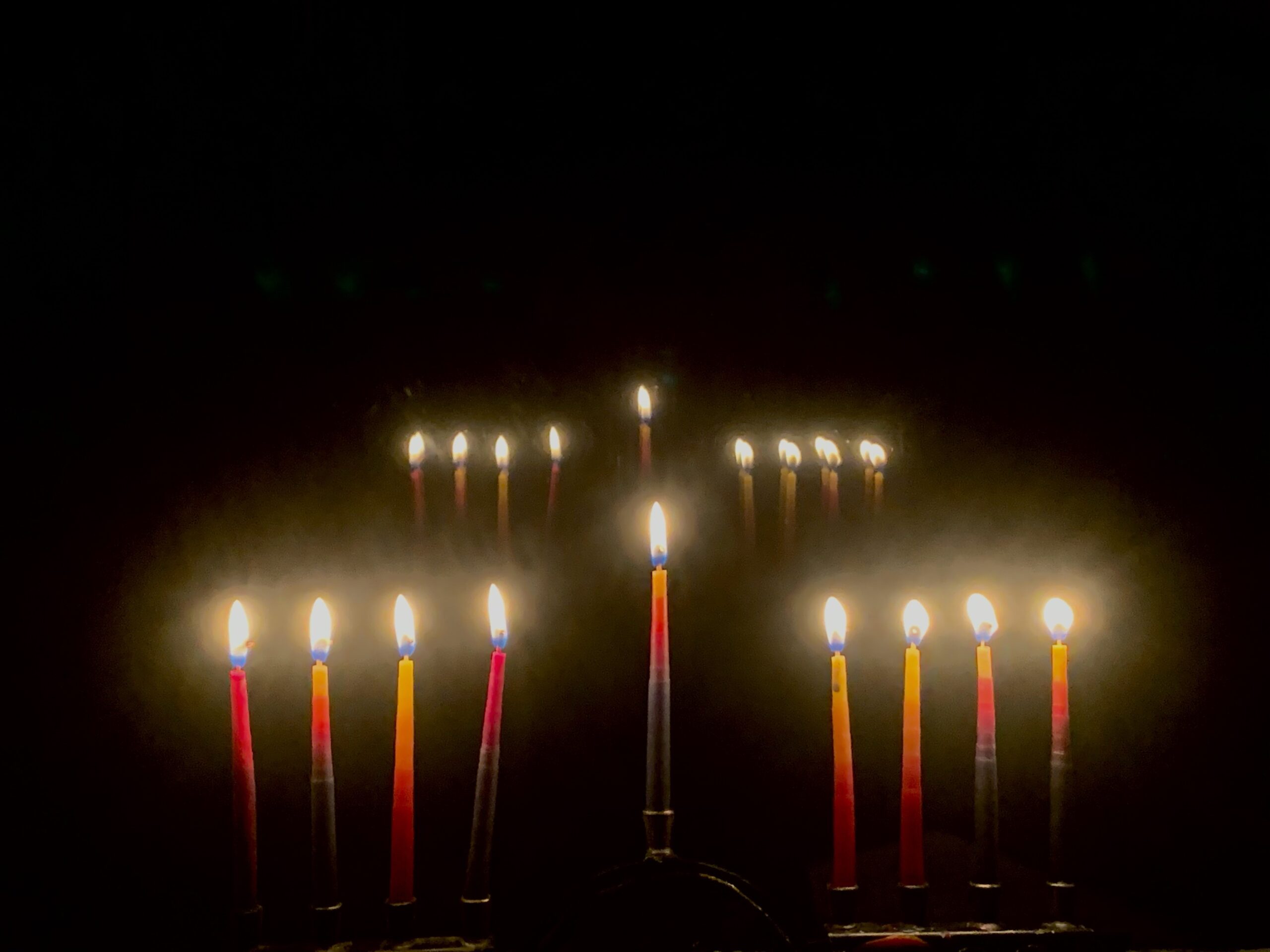 fully lit hanukkiyah in the dark with another hanukiyah in the background that appears to be a reflection of the first