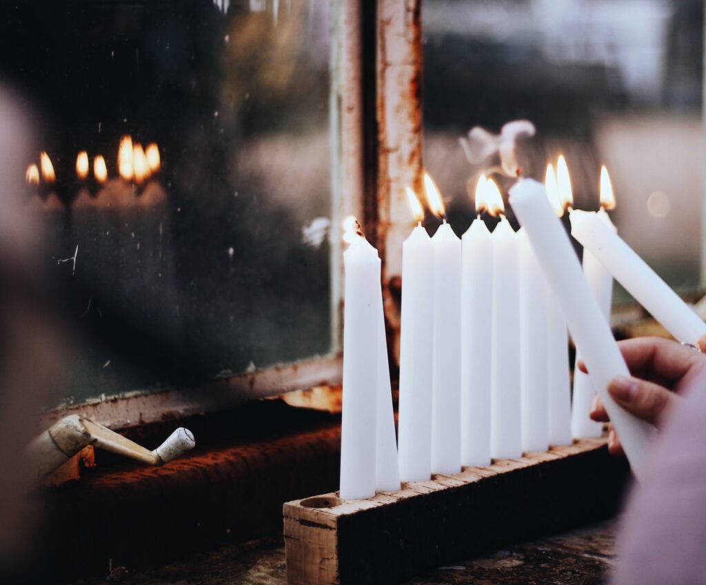 lighting all white hanukkah candles in window with reflection of candles