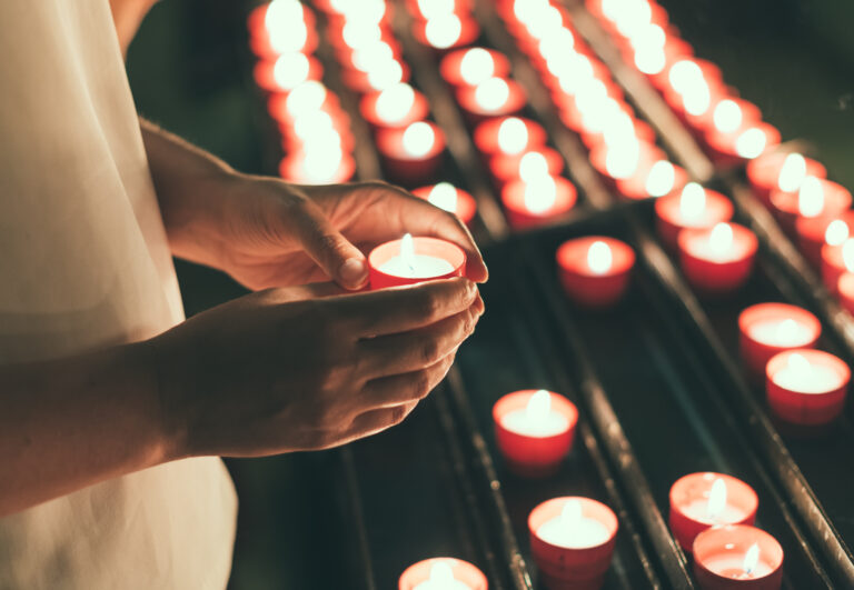 person holding lit tea light candle near rows of other lit tea lights