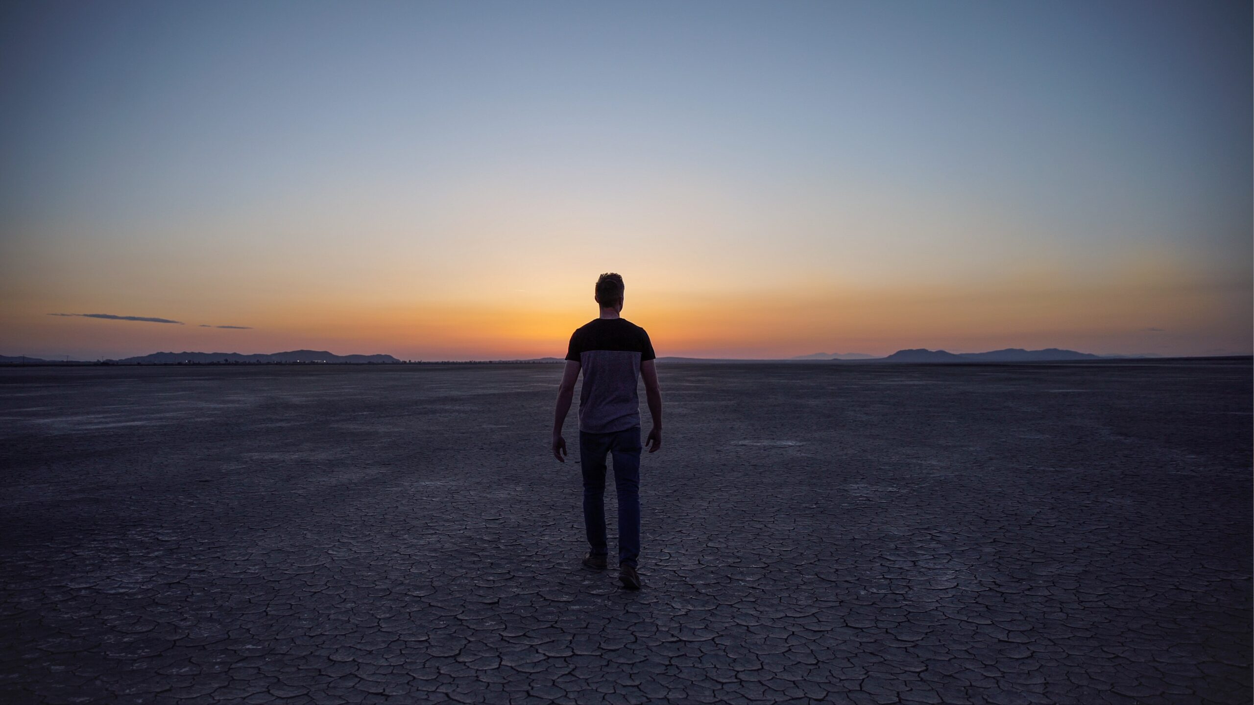 silhouette of person walking in desert toward sunset