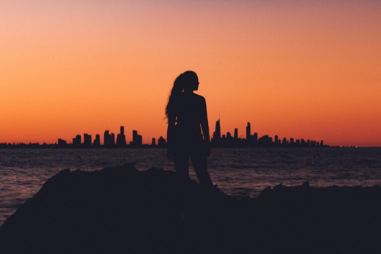 silhouette of woman looking to the right against orange sunset overlooking city