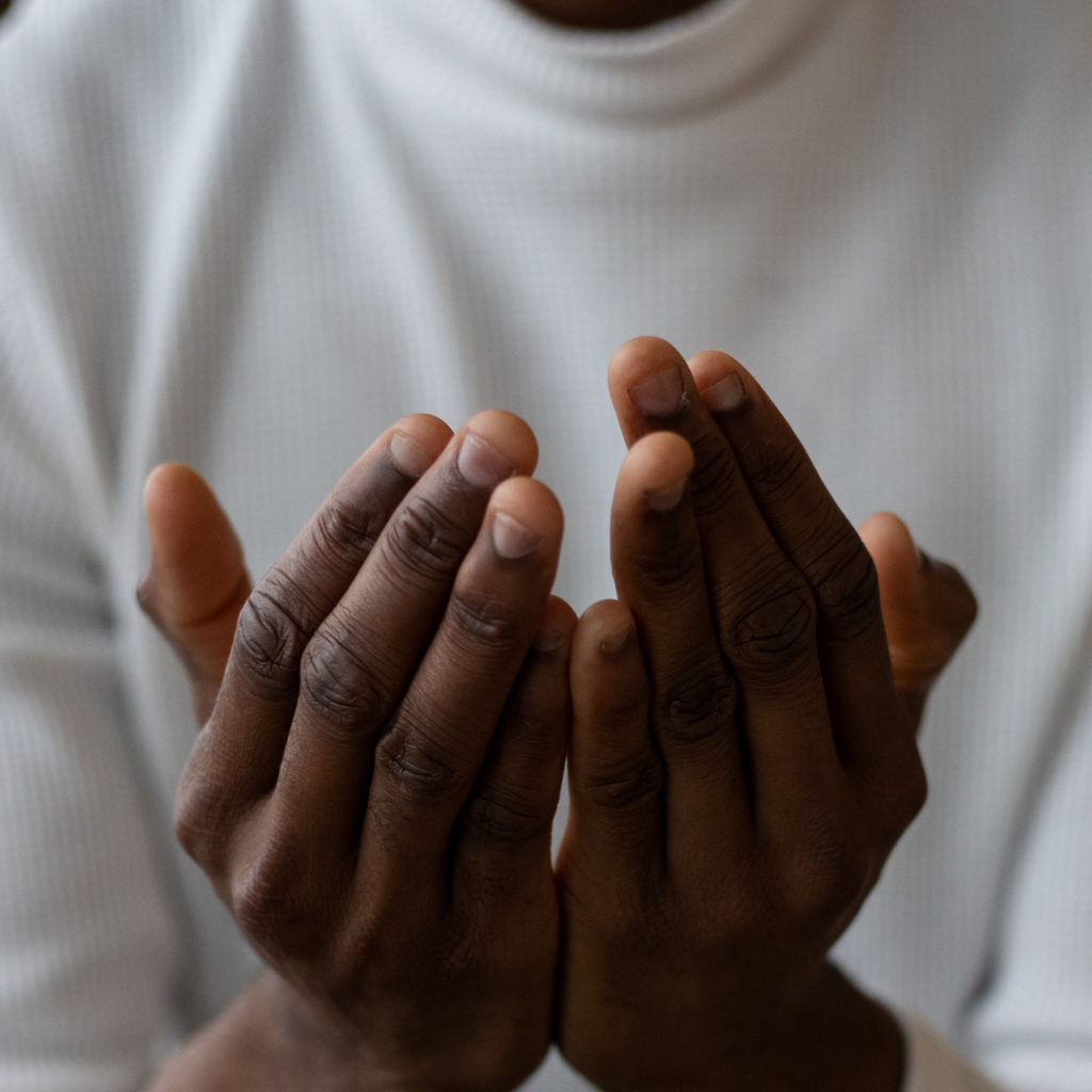 Two hands held in a prayer form, cupped like, of an african american person wearing a white shirt