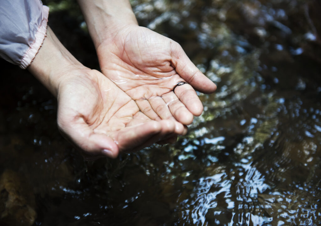 white hands cupping water over a body of water