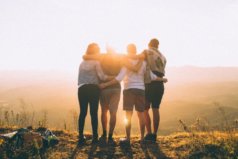 four friends arm in arm standing in sunlight out in nature