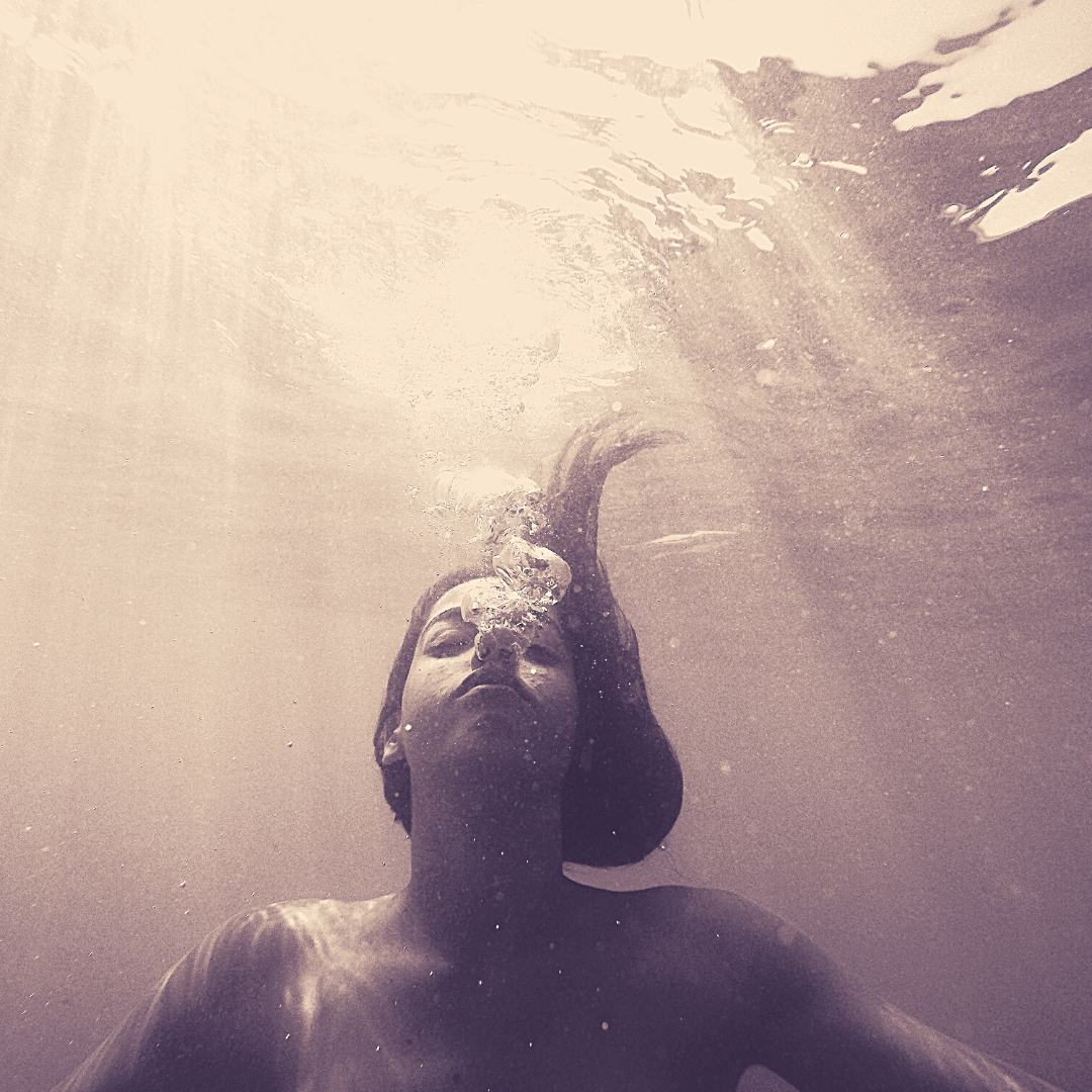 sepia toned photo of woman submerged in water with light filtering from above