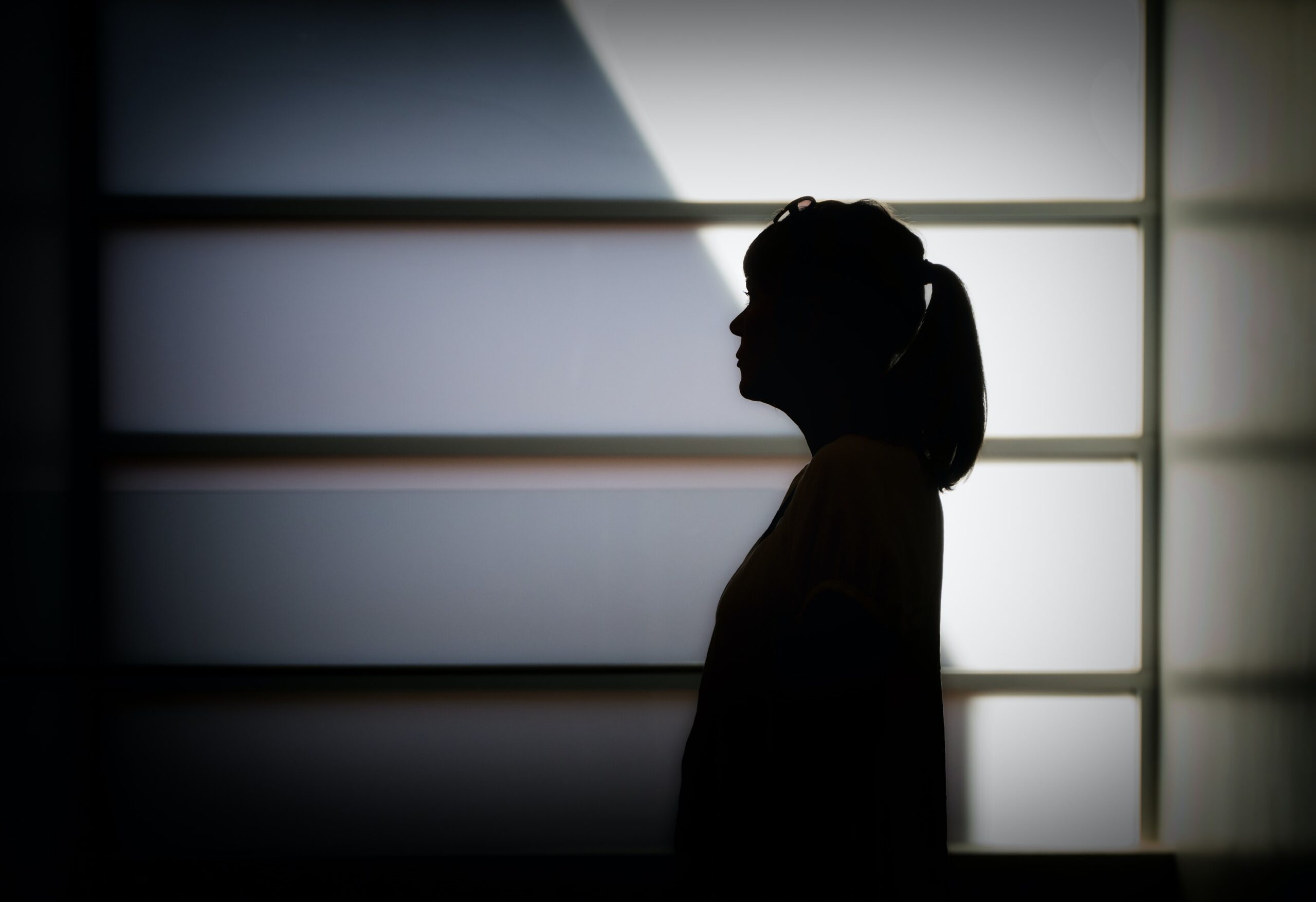 a woman in a ponytail silhouetted against a white wall