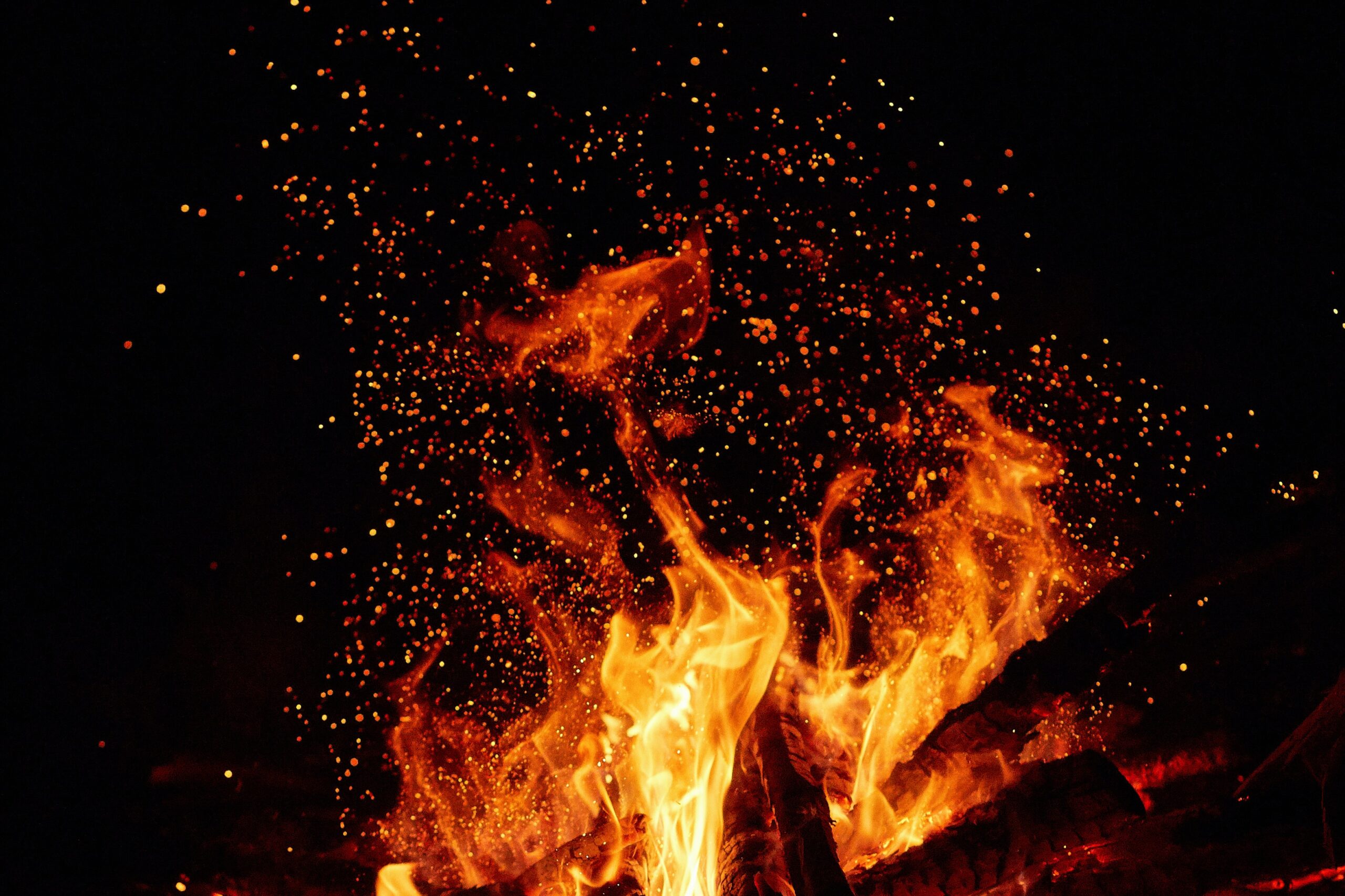 close up of bonfire flames with orange sparks flying in the air against black background
