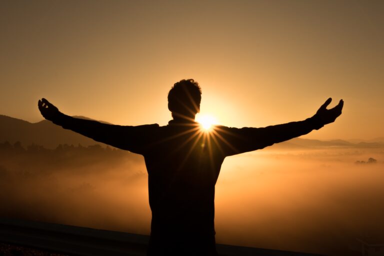 man with outstretched arms silhouetted from behind, facing the sunrise