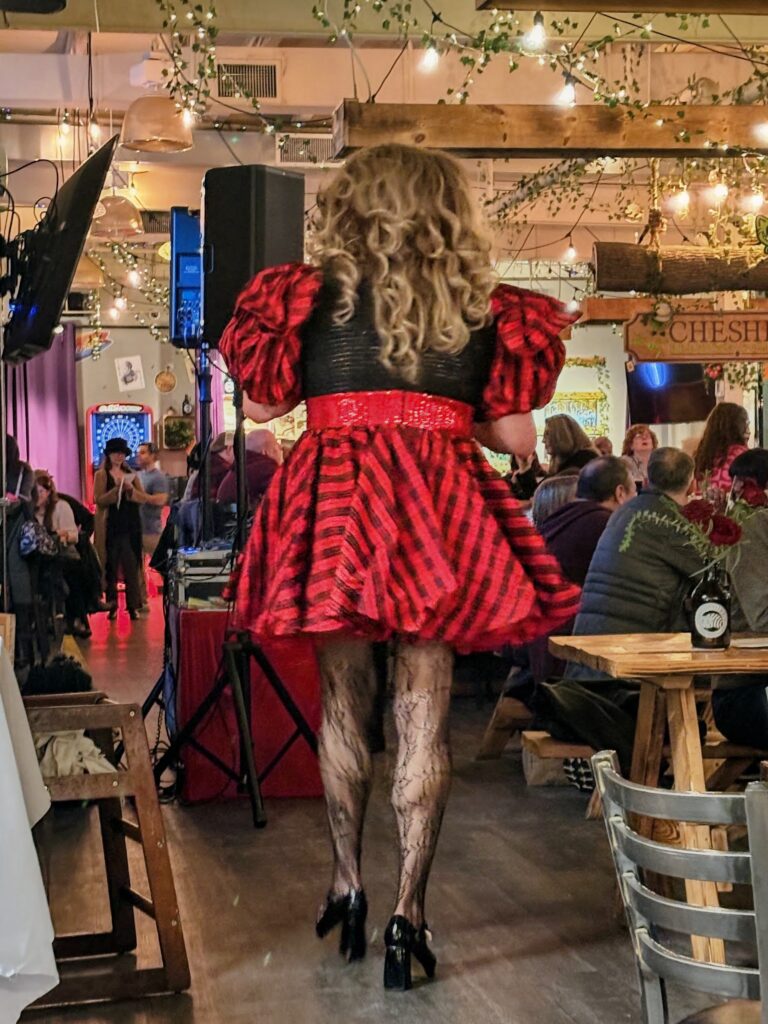 Person in a red and black dress with curly hair performing in a lively, crowded restaurant or bar.