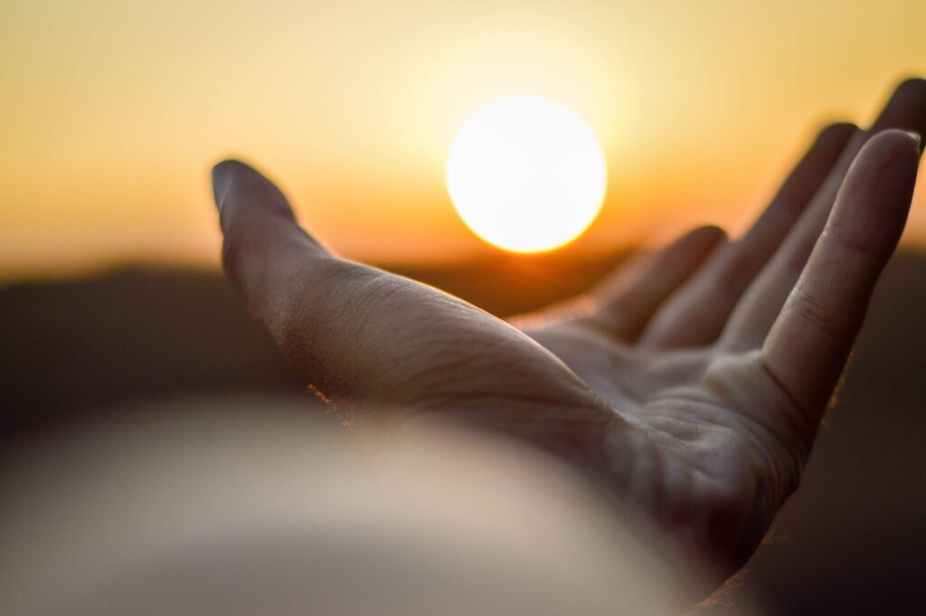 open hand in the foreground, sun setting in the background