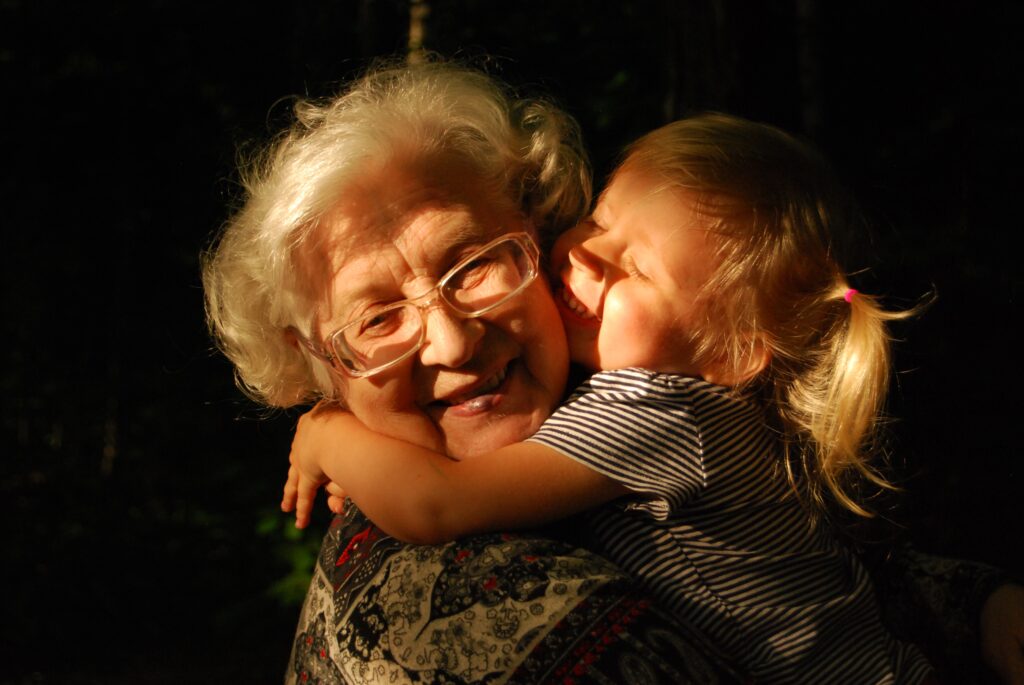 Smiling grandmother being hugged by toddler in pigtails against a black background
