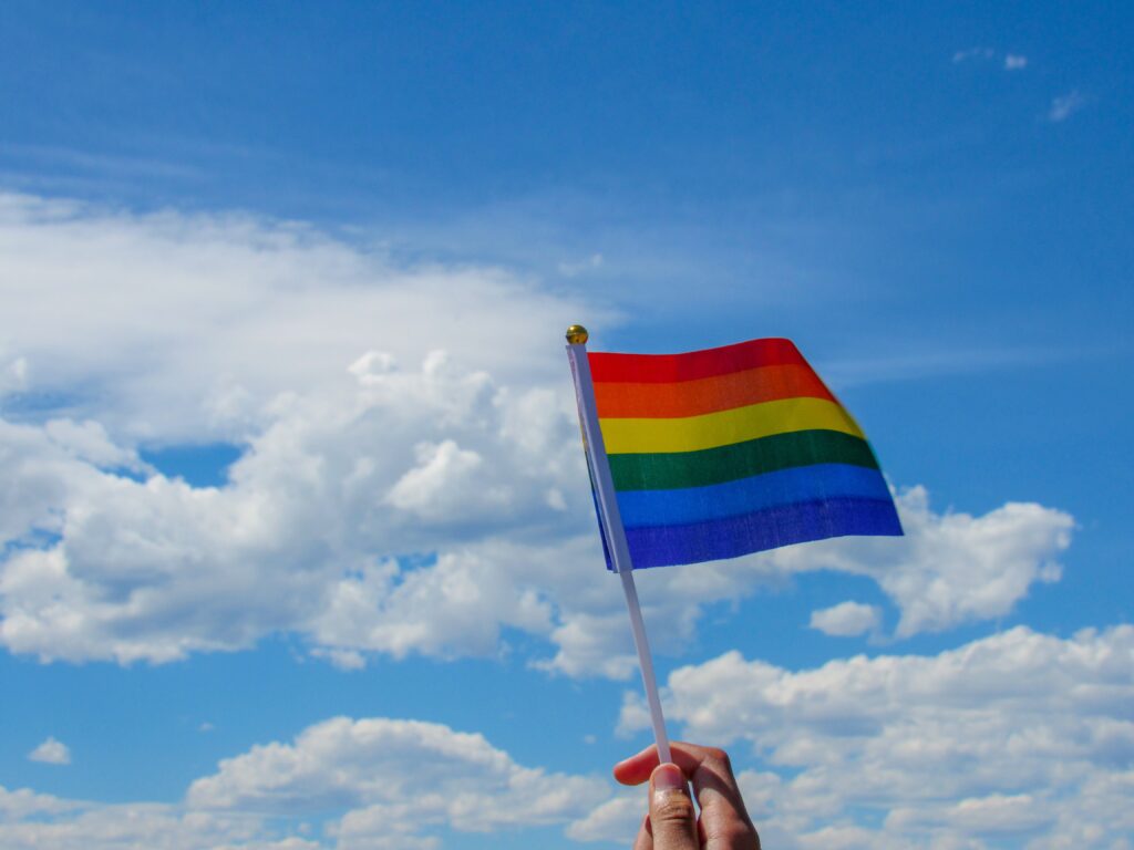 pride flag against a blue sky with white clouds
