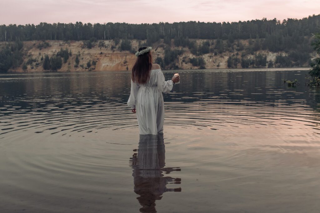 woman standing a lake wearing a flower crown and holding a lit candle