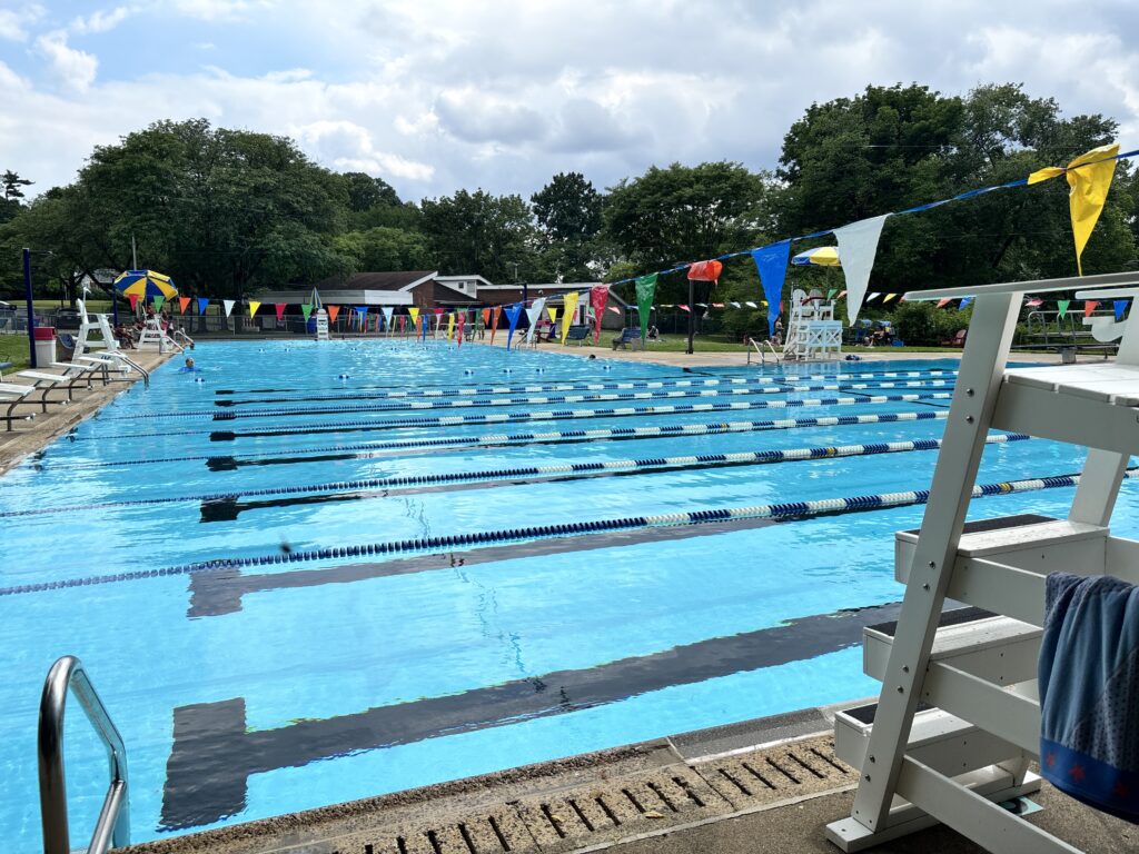 Outdoor swimming pool with swim lanes, lifeguard chair, and colorful flags hanging above the water.