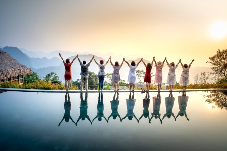 row of people holding hands with arms raised in front of a pool of water reflecting their image