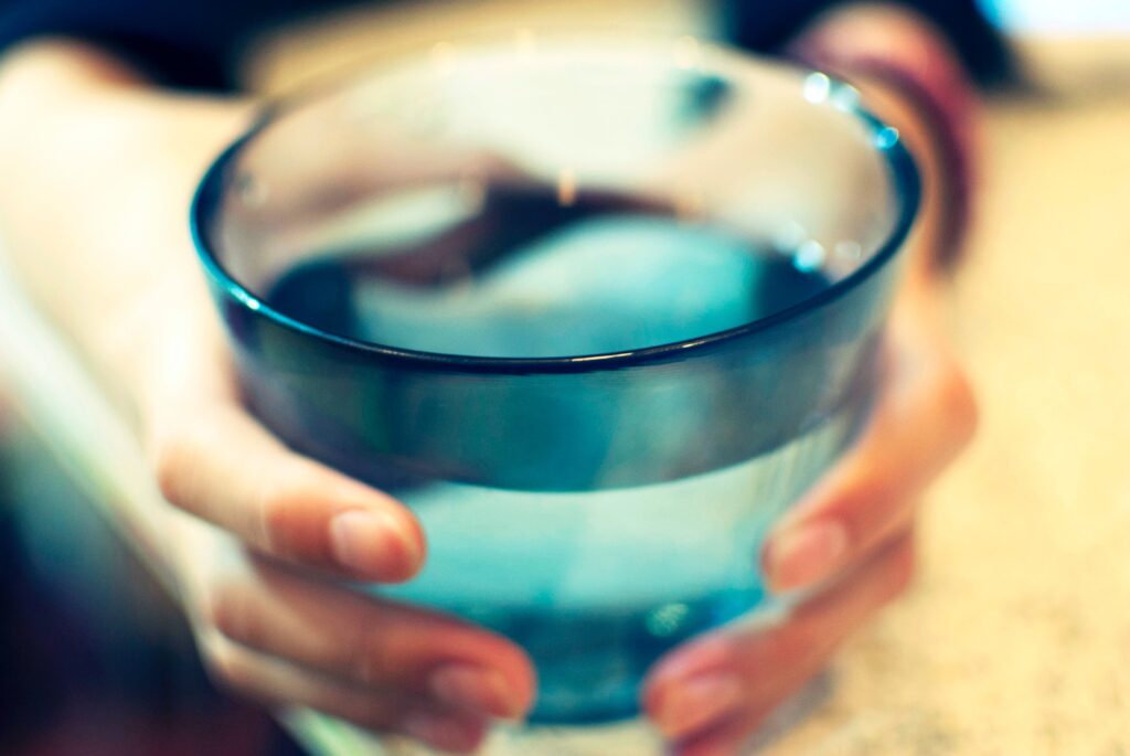 White-skinned hands grasp a glass of blue water