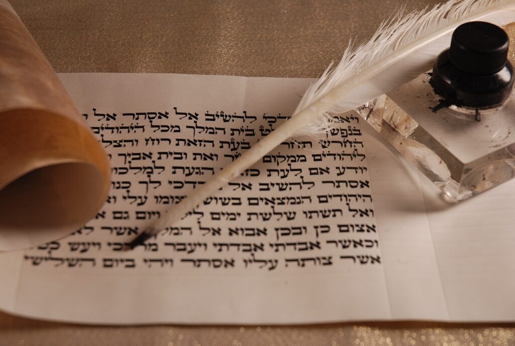 a scroll with Hebrew letters, part of Megillat Esther, with a quill and bottle of ink.