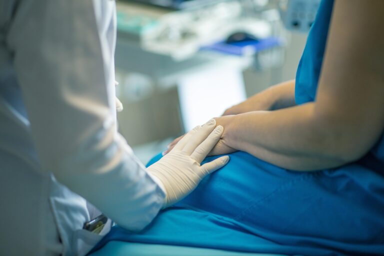 a person who is wearing a lab coat and latex gloves rests their hand on the hand of a person wearing a dress