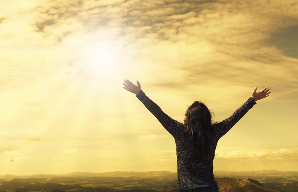 a woman opens her arms towards the sunny sky