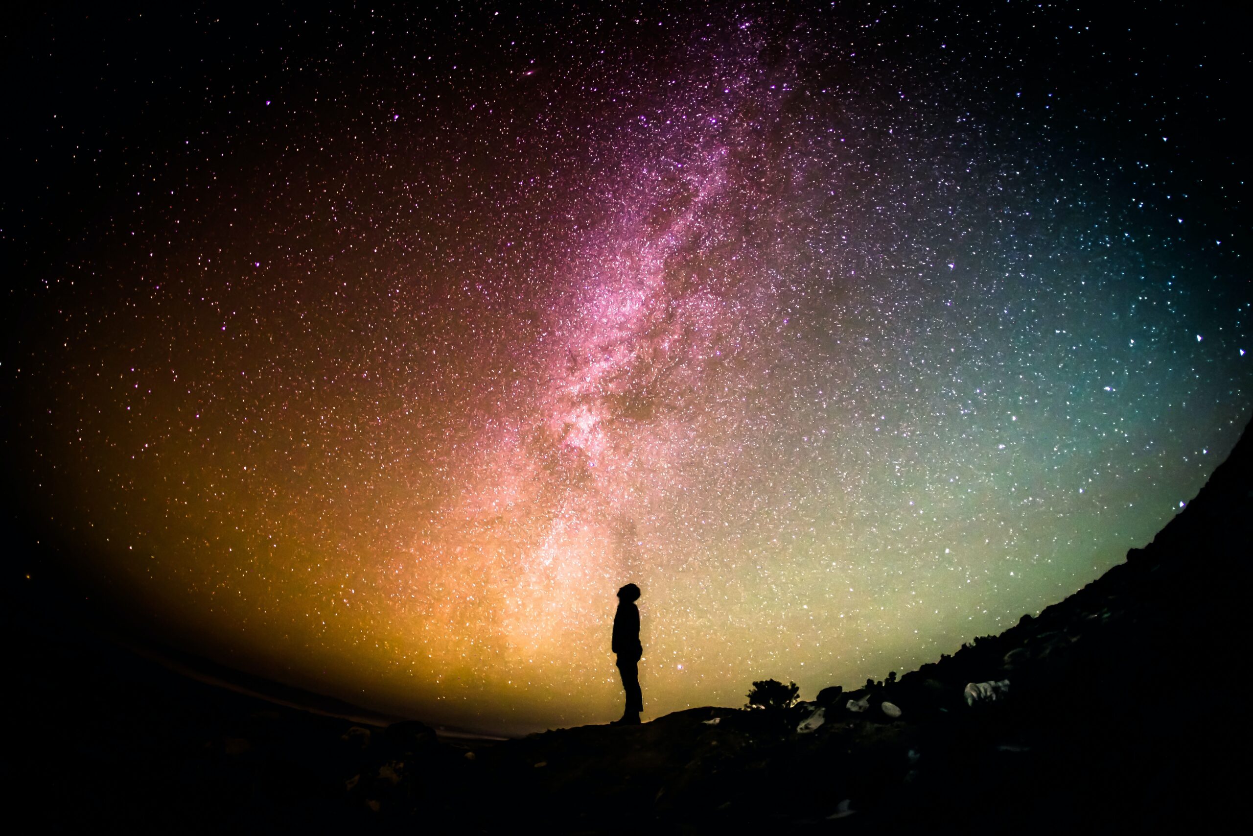 a person stands looking into a sky full of pink and green clouds