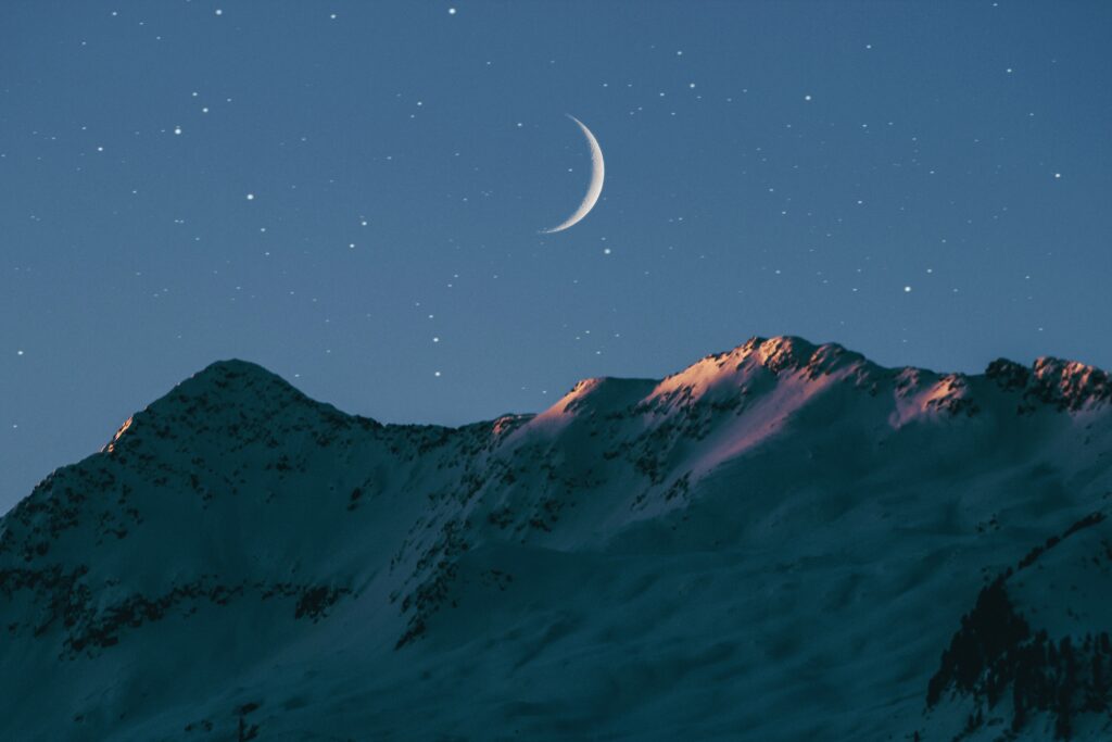 the moon looms over the mountains in a deep blue sky