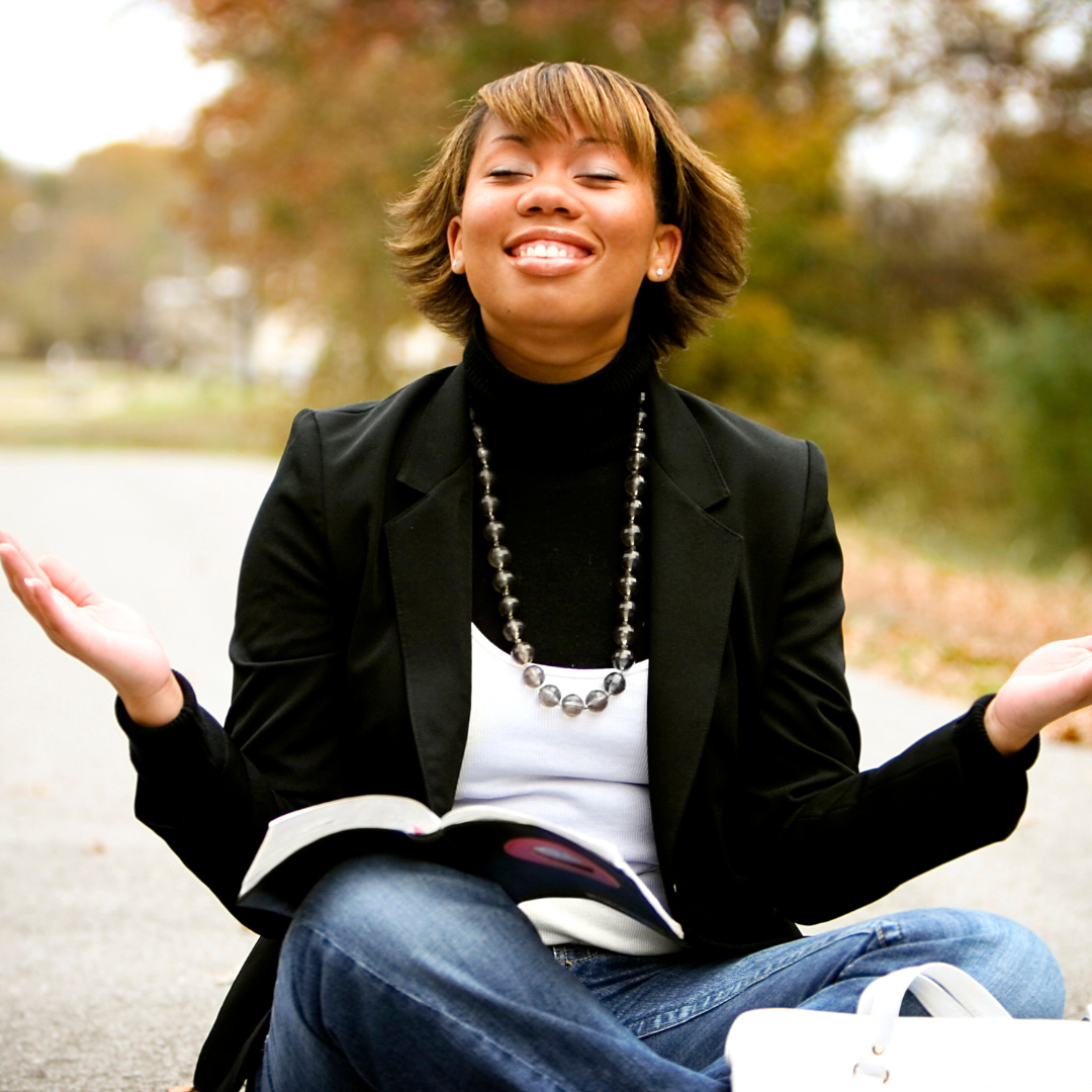 a woman sits with her hands up, smiling, a journal in her lap