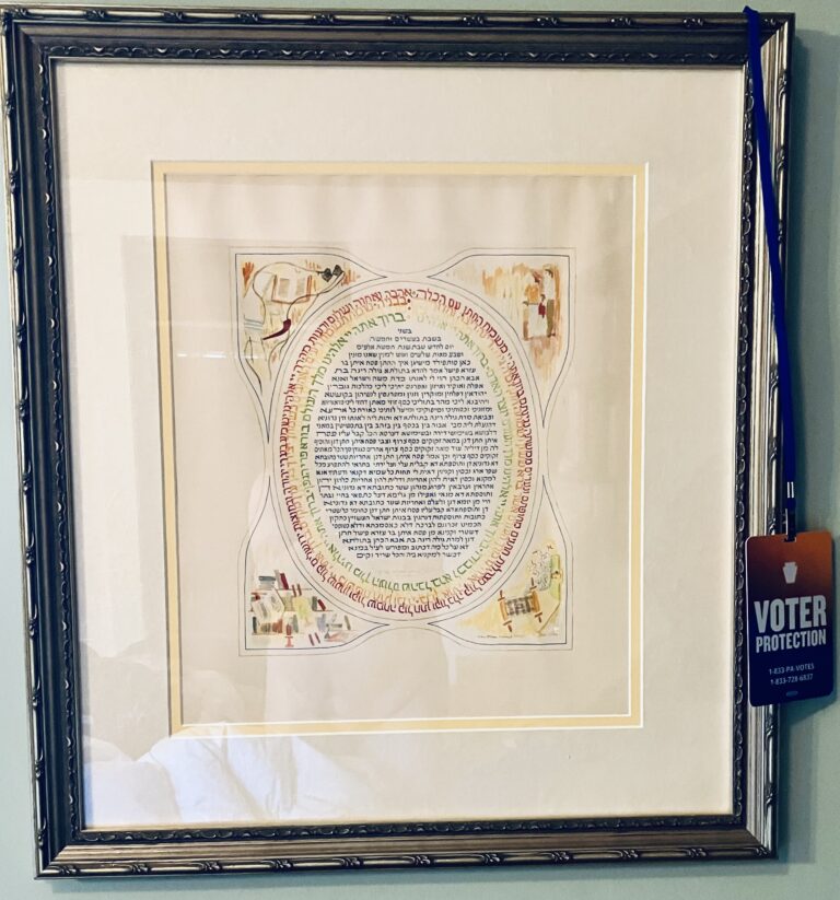 a ketubah with a voting badge hanging on the frame