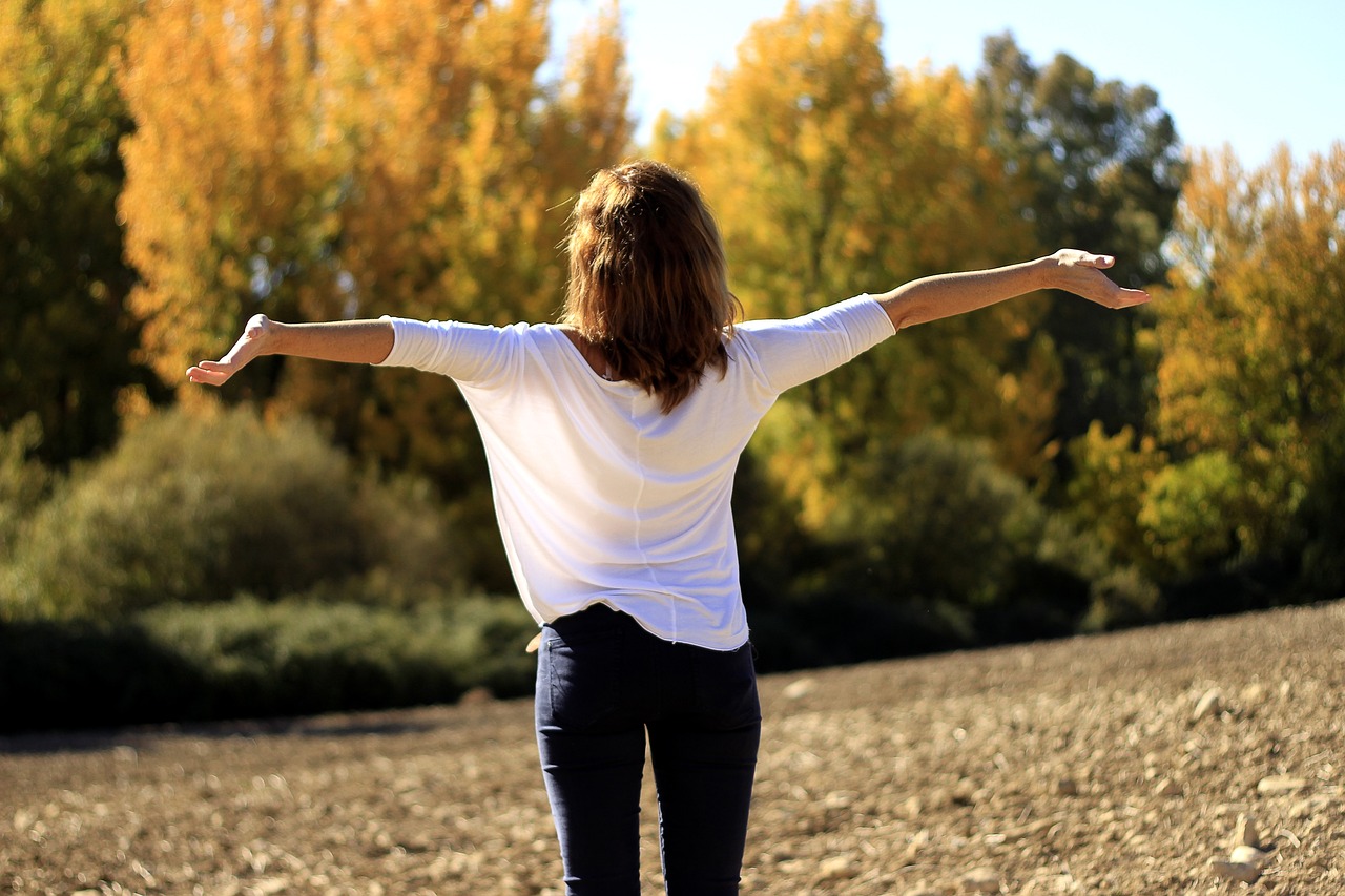 a woman spreads open her arms to the sky. She is standing ina. field